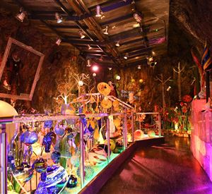 A colorful room with artistic glass sculptures and colored light. The walls are made of rock, creating a unique atmosphere.