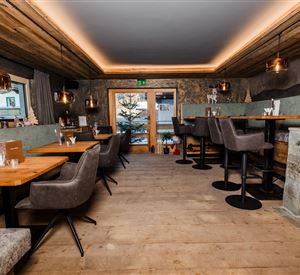 Ein modernes Restaurant mit Holzböden und gemütlichen Sitzplätzen. Große Fenster bieten einen Blick nach draußen auf einen Baum.