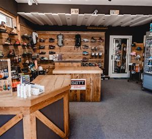 A sporting goods store with wooden shelves displaying various shoes and equipment. Care products and small accessories are on the counter.