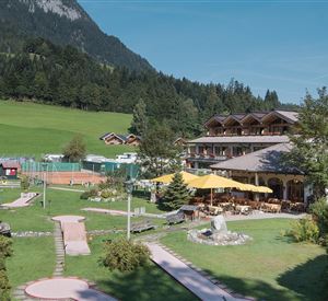 Eine malerische Hotelanlage mit einem gepflegten Garten und einem Minigolfplatz. Im Hintergrund sind grüne Wiesen und majestätische Berge zu sehen.