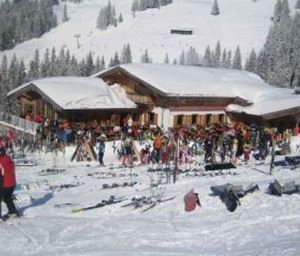 Een druk skihutgebied in de sneeuw met veel skiërs en ski-uitrusting. Op de achtergrond zijn besneeuwde bomen en bergen te zien.