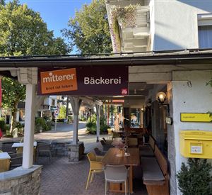 A cozy bakery with an inviting outdoor area. The surroundings are characterized by trees and sunny weather.