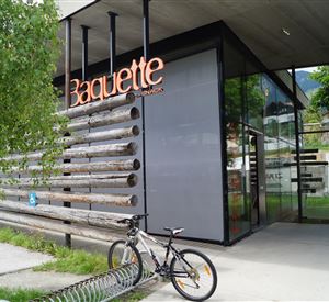 A modern shop with the sign "Baguette". Outside, there is a bicycle and a green area with trees.