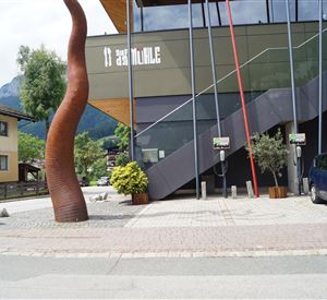 Een modern ontworpen gebouw met een aantrekkelijke sculptuur op de voorgrond. Op het trottoir zijn er elektrische oplaadpunten zichtbaar.