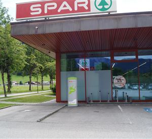 Een SPAR-supermarkt met grote ramen en een moderne inkomhal. Op de achtergrond zijn bomen en een groene weide te zien.