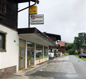 Ein Elektrogeschäft mit dem Namen "Salvenmoser" an einer ruhigen Straße. Im Hintergrund sind typische alpine Gebäude und ein bewölkter Himmel zu sehen.