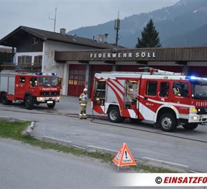 Twee brandweerwagens staan voor het brandweerkantoor in Söll. Op de achtergrond zijn bergen en een landelijke omgeving te zien.