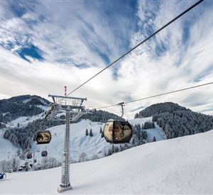 Eine Seilbahn fährt über verschneite Berge. Der Himmel ist teilweise bewölkt und die Landschaft ist winterlich schön.
