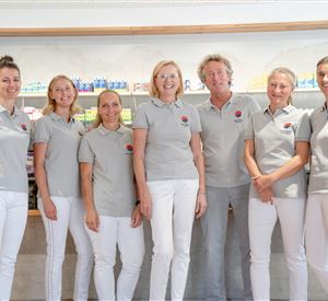 Een team van zeven personen staat voor een rek met gezondheidsproducten. Iedereen draagt grijze poloshirts en witte broeken.