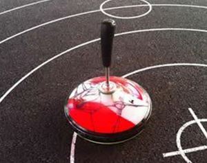 A colorful spinning top stands on a sports field with black lines. The ground has various field markings.