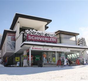 A modern ski rental shop in a snowy winter landscape. The facade features large windows and an inviting sign that reads "Ski Rental".