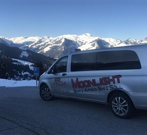 Ein silberner Van steht auf einem Parkplatz mit schneebedeckten Bergen im Hintergrund. Die Umgebung ist winterlich und sonnig.