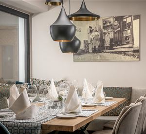 Een gezellig restaurant met een mooi gedekte tafel en elegante stoelen. Boven de tafel hangen stijlvolle lampen en er is een vintage schilderij aan de muur.