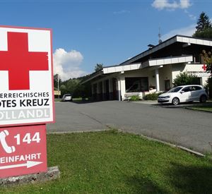 A building of the Austrian Red Cross in Söllandl. In the foreground is a large red cross sign with the phone number 144.