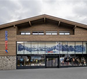 Een modern gebouw met houten gevelbekleding en grote ramen. Op de achtergrond is een bergmotief te zien.