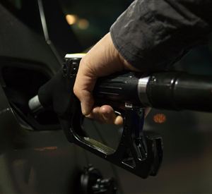 Een hand houdt een benzineslang vast die in de tank van een auto is gestoken. Het is donker, en op de achtergrond zijn vage lichten zichtbaar.