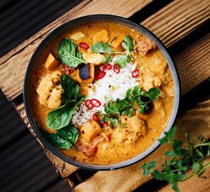 Een kleurrijk curry-gerecht met groenten, verse spinazie en rode chilipepers. Geserveerd met rijst in een eenvoudige kom op een houten tafel.