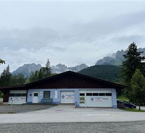 A modern building in a natural environment, surrounded by trees and mountains. The sky is cloudy and there is a calm atmosphere.