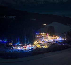 Een feestelijk verlichte winterlandschap met een klein dorpje te midden van met sneeuw bedekte bomen. De lichten creëren een gezellige sfeer in de nacht.