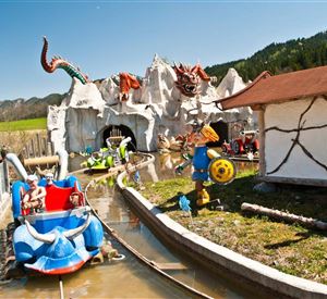 Een pretpark met een waterbaan en kleurrijke figuren. Op de achtergrond zijn bergen en een blauwe lucht te zien.