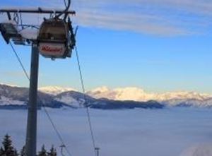 A cable car travels over a snow-covered landscape with mountains in the background. Below, a sea of fog spreads out.