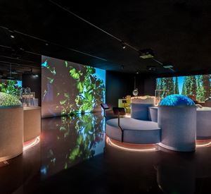 Een modern interieurontwerp met interactieve elementen en projecties van natuurlijke motieven. Er zijn ronde zitmogelijkheden en een gedempte verlichting.