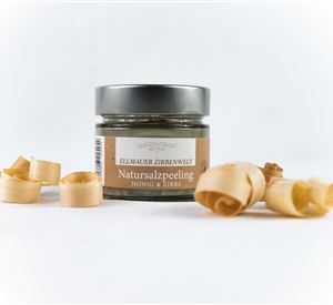 Een glas met natuurzoutscrub staat op een witte achtergrond. Naast liggen enkele houtspaanders.