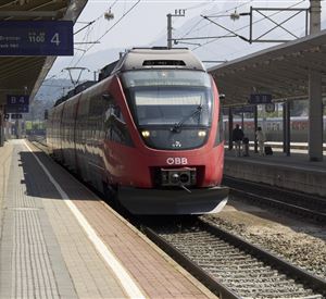 Een rode trein van de ÖBB staat op het station. De sporen zijn zichtbaar en de architectuur van het station is modern.