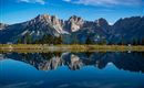 Eine beeindruckende Berglandschaft mit klaren Gipfeln, die sich im ruhigen Wasser spiegelt. Der Himmel ist blau und wolkenlos.