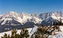 Eine beeindruckende Berglandschaft mit schneebedeckten Gipfeln und klarem blauen Himmel. Im Vordergrund steht ein Holzgeländer, das einen schönen Blick auf die Umgebung bietet.