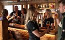 A cozy bar with cheerful guests and friendly staff. The wooden decor creates an inviting atmosphere.
