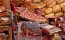A market table with various sausage and meat products. In the background, many bread rolls can be seen.
