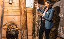 Eine Frau steht in einem Bergwerk und erklärt eine Informationstafel. Um sie herum sind Holzelemente und Bergbaugeräte sichtbar.