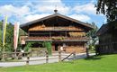 Ein traditionelles Holzhaus mit Balkonen und Blumen. Der Garten ist grün und ein Zaun umgibt das Grundstück.