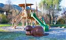 A playground with a large wooden slide and a slide mountain. In front of the slide, there is a playful, brown animal.
