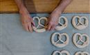 Een bakker vormt pretzels van deeg. De pretzels liggen op een bakplaat.