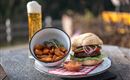 A juicy hamburger with fresh vegetables on a plate. Accompanied by crispy potato pieces and a beer in a glass.