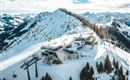 A picturesque mountain landscape with snow-covered peaks. In the foreground, a mountain station and chairlifts can be seen.
