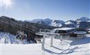 A wintry mountain landscape with snow-covered mountains and a gondola. The sky is clear and sunny.