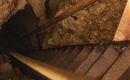 A steep metal staircase leads into a dark cave. The floor is covered with stones and earth.