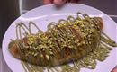 A freshly baked croissant on a plate, garnished with green drizzle and chopped pistachios. The dessert looks appetizing and tempting.