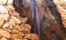 A cave with large rocks and stalagmites. A person with a red helmet is exploring the room.