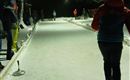 Eine verschneite Eisbahn bei Nacht mit beleuchteten Bereichen. Einige Personen sind beim Spielen aktiv.