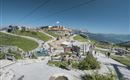 A picturesque mountain village with many visitors and clear blue sky. The surroundings are green and inviting, ideal for outdoor activities.