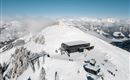 A snow-covered mountain landscape with a modern mountain station and lifts. Many people enjoy winter activities in the beautiful surroundings.