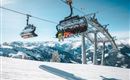A cable car travels over snow-covered mountains. The sky is clear and sunny.
