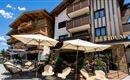 Ein modernes Hotel mit einem einladenden Außenbereich und Sonnenschirmen. Die Architektur kombiniert Holz- und Glaselemente und vermittelt eine gemütliche Atmosphäre.