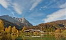 An idyllic landscape with a clear lake and colorful autumn foliage. In the background, majestic mountains and a blue sky can be seen.