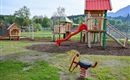 A playground landscape with wooden play equipment and a slide. In the foreground, there is a seesaw shaped like a horse.