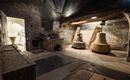 Ein historischer Glockenturm mit zwei großen Glocken. Der Raum hat eine rustikale, steinerne Atmosphäre und eine Tür, die zu einem weiteren Bereich führt.